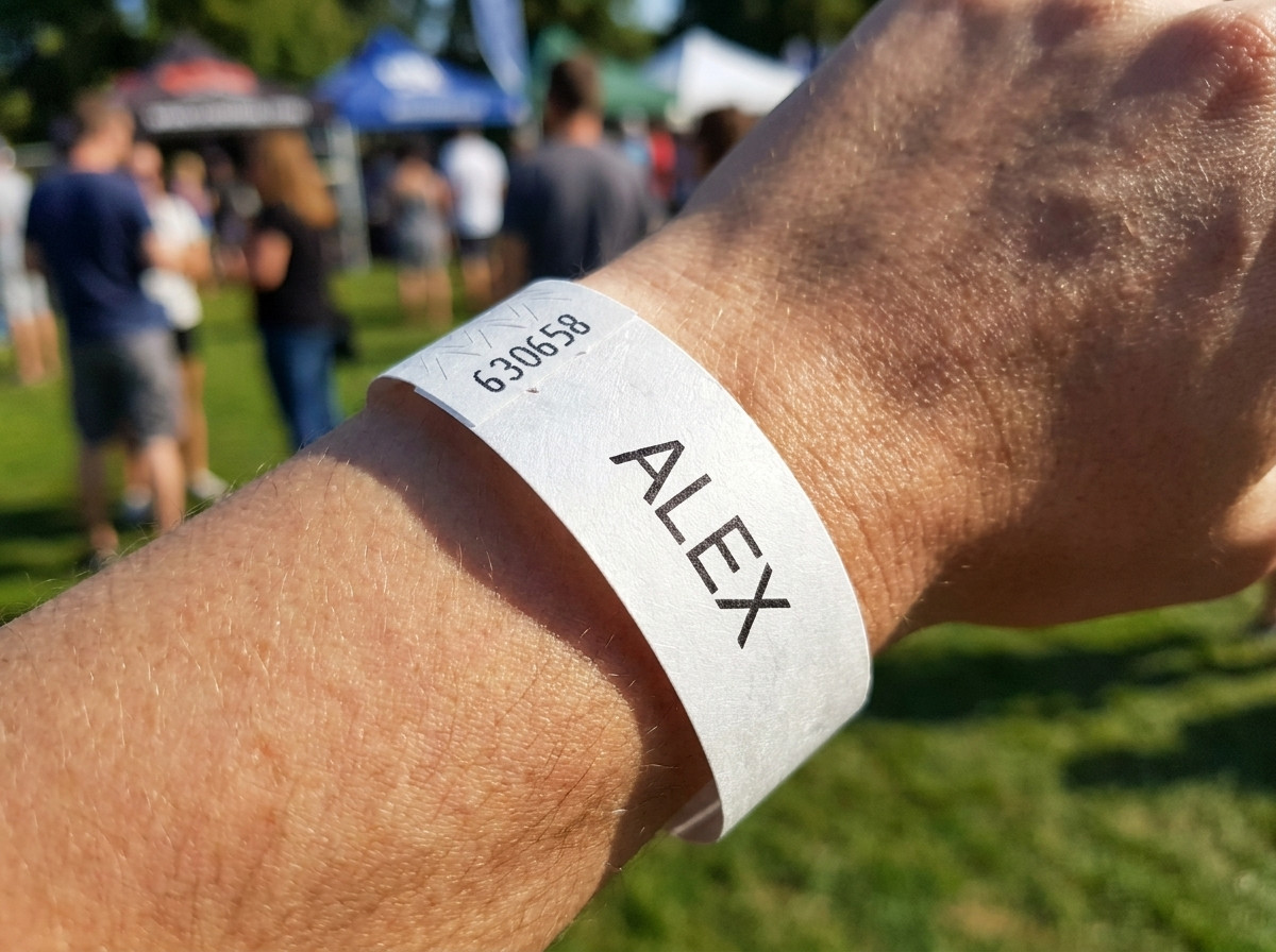 Wit Tyvek-armband bedrukt met de voornaam van een kind en een noodnummer, gedragen om de pols van een jong kind tijdens een openluchtgebeurtenis