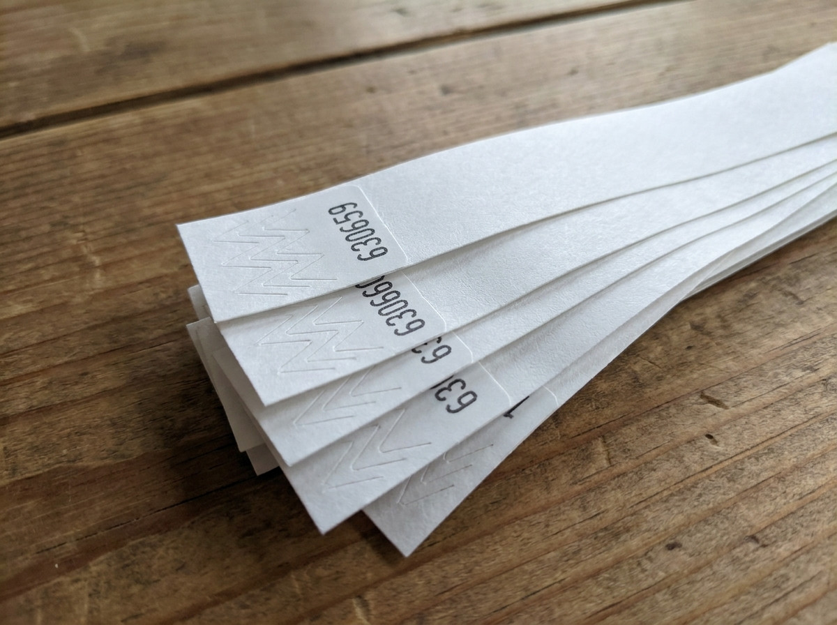 Close-up van Tyvek polsbandjes met sequentiële nummering gedrukt in zwart, waaiergewijs uitgelegd op een toegangscontrole tafel tijdens een evenement